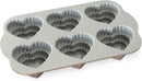 Toffee-colored Nordic Ware cakelet pan with six tiered heart-shaped cavities, displayed on a white background.