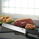 The Victorinox Fibrox Pro slicing knife being used to carve thin slices of ham on a black cutting board.