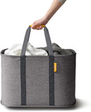 A gray Joseph Joseph Hold-All Max collapsible laundry basket with a yellow tag and gray fabric handles. The basket has a moisture-resistant black interior.