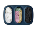 A dark blue Joseph Joseph Tota Trio laundry hamper with three separate internal compartments, each with a handle. The gray lid is propped against the side of the hamper.