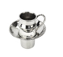 A hammered silver metal cup with a beaded design on the rim of the cup, handle, and a matching saucer. The cup sits on a small, round base.
