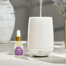 The Trapp No. 77 Palo Santo Ultrasonic Diffuser Oil placed next to an active white ultrasonic diffuser, showcasing its intended use.