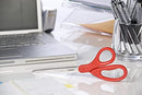 Red scissors on a cluttered desk next to laptop and pens