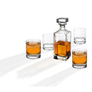 A crystal whiskey decanter with four matching glasses arranged neatly on a white background.