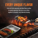 Grilling and serving set by Yukon Glory, featuring a large silver pan and three smaller black grill/sear trays with cooked food, plus a handle, all next to its product packaging.