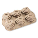 Toffee-colored Nordic Ware cakelet pan with six tiered heart-shaped cavities, displayed on a white background.