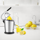 A brushed stainless steel citrus juicer with a black handle, actively juicing an orange into a glass of orange juice.