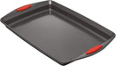 Angled view of a gray nonstick cookie pans with bold red silicone grips, shown on a white background.