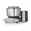 A Bosch Universal Plus stand mixer with a stainless steel bowl and a black base. The mixer has a white control panel with a knob for adjusting settings, and the Bosch logo is visible. A clear splash guard is on top of the bowl, and the motor housing is black with a silver vertical accent.