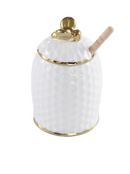 A white, textured ceramic honey pot with a gold rim around the base and lid. The lid has a gold bee-shaped handle. A light wooden honey dipper extends from an opening in the lid. The background is a transparent checkerboard pattern.