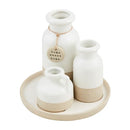A decorative set featuring a round, speckled stoneware tray holding three white and natural tan ceramic vases of varying shapes, one of which has a tag reading "home sweet home."