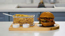 Yukon Glory Burger Serving Set, featuring a wooden board with a metal fry basket, two ceramic ramekins for sauces, and a burger on a round black coaster.