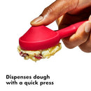 Three OXO Good Grips silicone cookie scoops stacked on a white background. The scoops have gray, red, and black silicone heads and matching comfortable handles with the OXO logo. The gray scoop has a sweep attached.