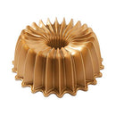 Gold Nordic Ware Brilliance Bundt pan with sharp, sculpted ridges and a circular shape, displayed on a white background.