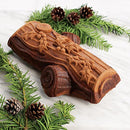 Chocolate sponge cake baked in a yule log mold with visible bark-like detailing, decorated with holly for a festive holiday presentation.