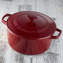 A red enameled cast iron round casserole with matching lid and wide handles, shown on a wooden table
