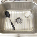 A rectangular sink protector grid in an almond color, designed to fit in a kitchen sink, with a central oval cutout for the drain and slightly raised feet.