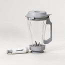 A clear plastic blender jar with a gray handle, gray lid, and integrated blade, shown next to a white and gray vacuum pump for food preservation.