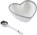 A white heart-shaped porcelain bowl with a silver beaded rim, accompanied by a matching white spoon. Dimensions of the bowl (5.5" x 5.5" x 2.5") and spoon (5" long) are indicated.