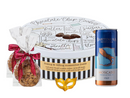 A large, themed gift set including a white tin printed with a chocolate chip cookie recipe, two cookies tied with a red bow, a blue can of Bartenura Moscato, and a small gold mask.
