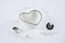 A white heart-shaped porcelain bowl with a silver beaded rim, accompanied by a matching white spoon. Dimensions of the bowl (5.5" x 5.5" x 2.5") and spoon (5" long) are indicated.
