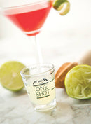 A clear glass shot glass with black measurement markings for ounces and liters, and the text "ONE SHOT" on the front.
