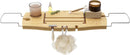 A light wood Umbra bathtub caddy with expandable metal arms, featuring a slotted book/tablet stand, a wine glass holder, and a recessed area with drain holes for soap or accessories.