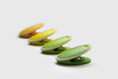 A set of four oval, plastic bag sealing clips in a tonal gradient of green and yellow colors. 