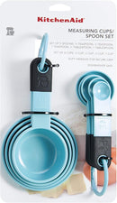 A set of nine light blue KitchenAid measuring cups and spoons with black soft-grip handles, spread out on a white surface. The set includes four cups and five spoons.