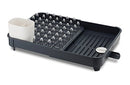 A gray Joseph Joseph Expandable Dish Drying Rack with a removable white cutlery holder and a plated steel wire rack for dishes. The rack is shown in its compact size.