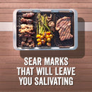 Grilling and serving set by Yukon Glory, featuring a large silver pan and three smaller black grill/sear trays with cooked food, plus a handle, all next to its product packaging.