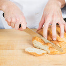 Chef using the Victorinox serrated bread knife to cut a loaf of fresh bread on a wooden surface.