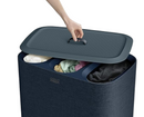 A dark blue Joseph Joseph Tota Trio laundry hamper with three separate internal compartments, each with a handle. The gray lid is propped against the side of the hamper.