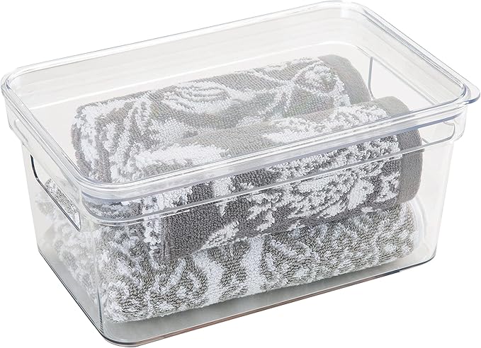 Small clear plastic storage bin with lid and open handles, containing towels, shown on a white background.