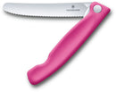 A bright pink Victorinox foldable knife with a serrated stainless steel blade shown partially open. The handle has an ergonomic shape.
