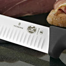 A detailed close-up of the Victorinox logo and Granton edge on the Santoku knife's stainless steel blade.