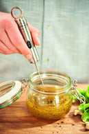 A person using the stainless steel milk frother to mix ingredients in a glass jar.