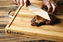 Babish Clef knife slicing cooked steak on wooden cutting board in kitchen setting
