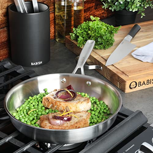 Babish stainless steel pan cooking steak and peas on a stovetop.