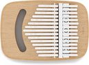 An elevated, side-angle view of an Umbra Strumba Kalimba. This musical instrument features a light-colored wooden top with a crescent-shaped sound hole and a series of white-tipped metal tines. The tines are engraved with musical notes or numbers. The base of the instrument is a smooth, rounded, off-white or cream color. The image is set against a plain white background. The "U umbra" brand logo is visible in the bottom right corner.