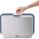 A set of three rectangular cutting boards in gray and white, stored vertically in a silver stand. The boards feature metal handles and non-slip feet.