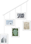 A contemporary white photo display featuring five square frames suspended from a horizontal bar by thin rods.