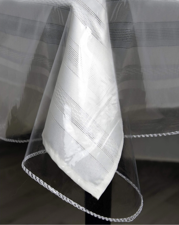 Close-up of a clear vinyl tablecloth protector, showcasing its transparency and how it overlays a patterned white tablecloth.