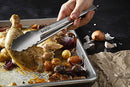 Hand using Babish stainless steel tongs to serve roasted chicken and vegetables from a sheet pan