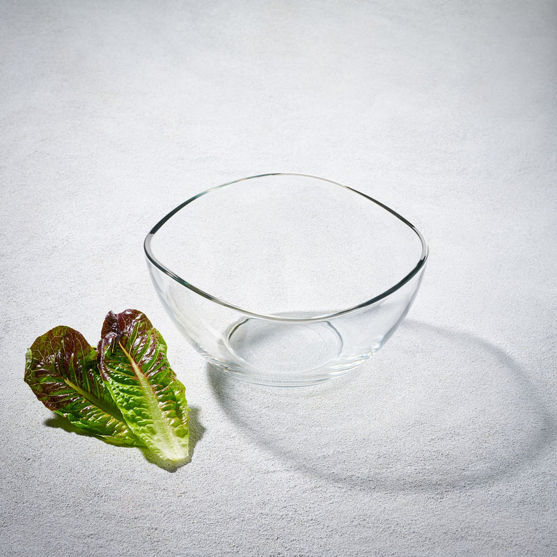 A LAV Vira 63.5-ounce clear glass bowl with a modern curved design, placed on a white surface next to a fresh lettuce leaf.