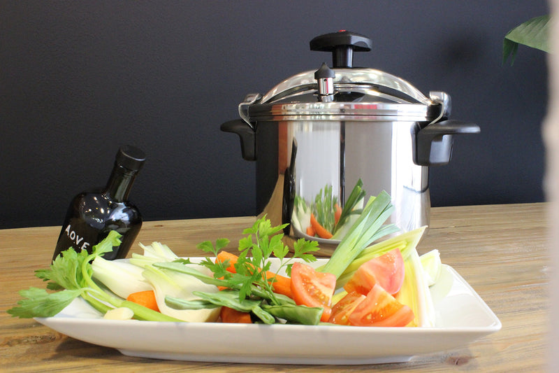 A plated meal with fresh vegetables next to the MAGEFESA Star pressure cooker, demonstrating its use in food preparation.