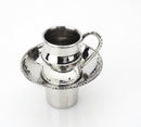A hammered silver metal cup with a beaded design on the rim of the cup, handle, and a matching saucer. The cup sits on a small, round base.