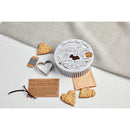 Contents of the Mud Pie Chocolate Chip Cookie Tin Set laid out, including the decorative recipe tin, metal heart cutter, black and white twine, brown paper bags, a printed recipe card with a vanilla pod, and several heart-shaped chocolate chip cookies.