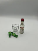 A gift set containing a mini bottle of Smirnoff vodka, a measuring shot glass labeled "ONE SHOT," and two green wrapped sour apple candies.