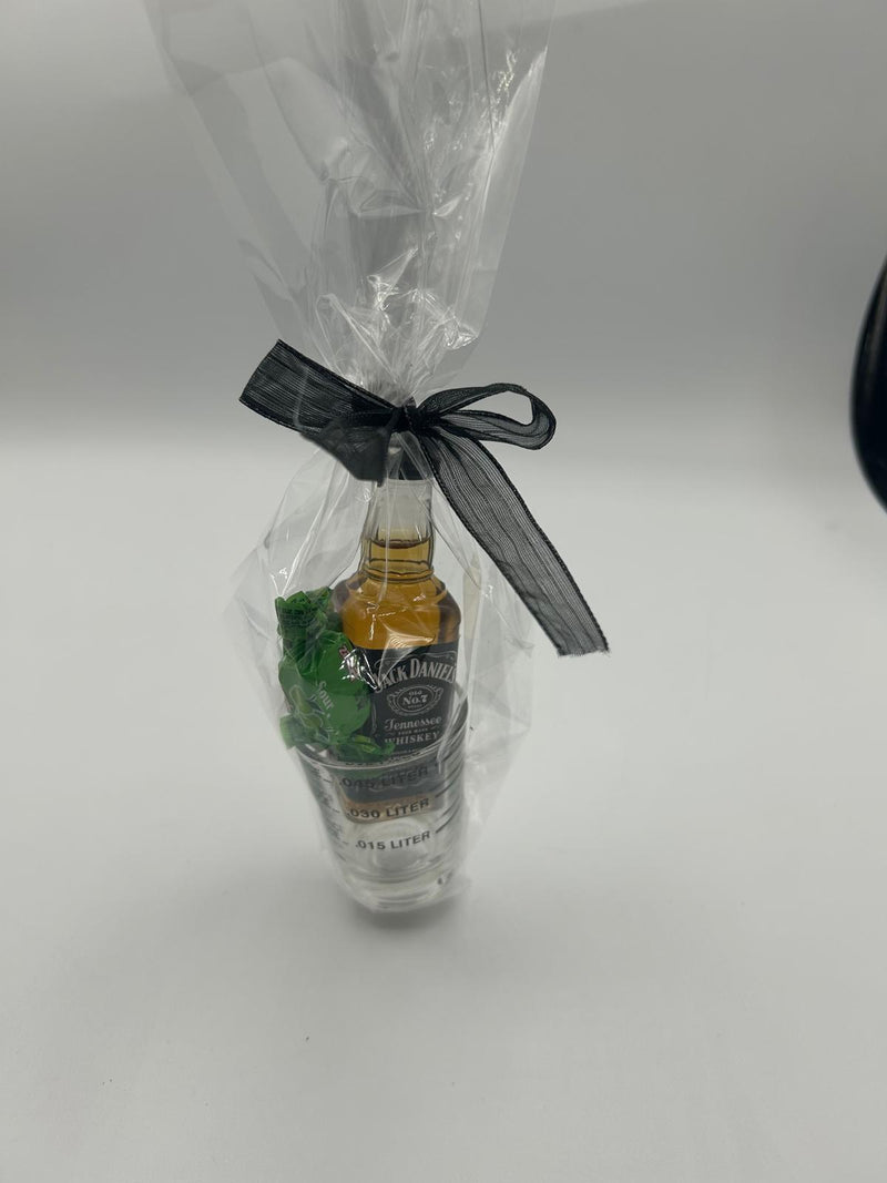 The Whiskey Business gift set wrapped in clear cellophane and tied with a black ribbon, showing the whiskey bottle, shot glass, and candies inside.